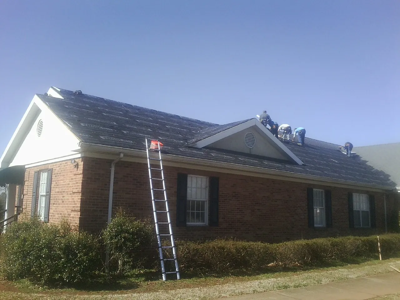 Crew tearing shingles off a brick ranch roof with a ladder set — Metal Roof Repair work by our crew in Tremont City