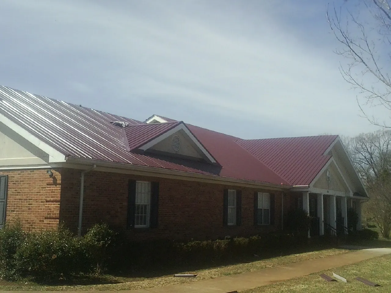Red metal roof with gabled entries on a long brick building, from a Hail Damage Roof Repair job in Tremont City