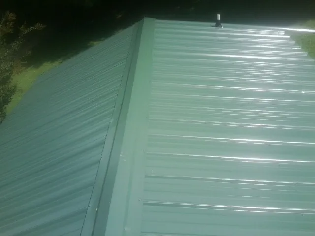 New green metal panels meeting at the ridge of a roof — Flat Roof Repair work by our crew in Tremont City