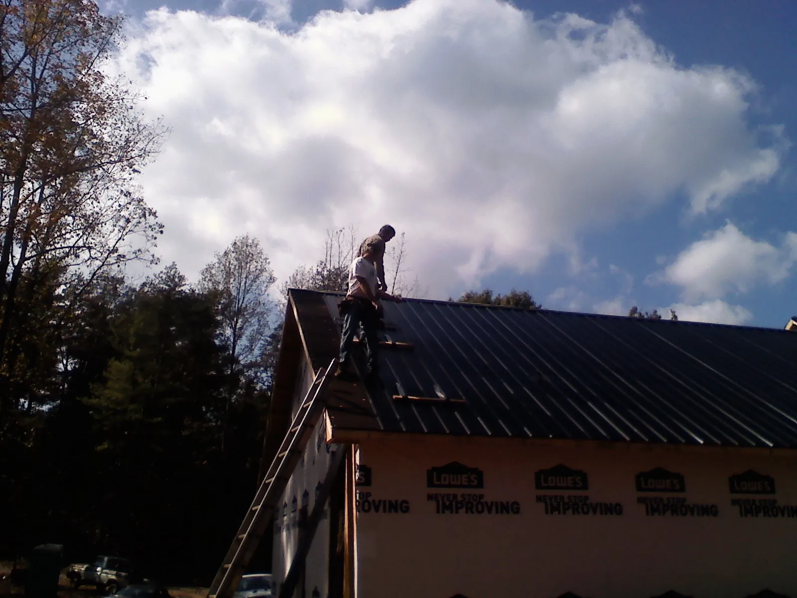 Roofer fastening dark metal panels high against a cloudy sky, from a Roof Inspection job in Tremont City