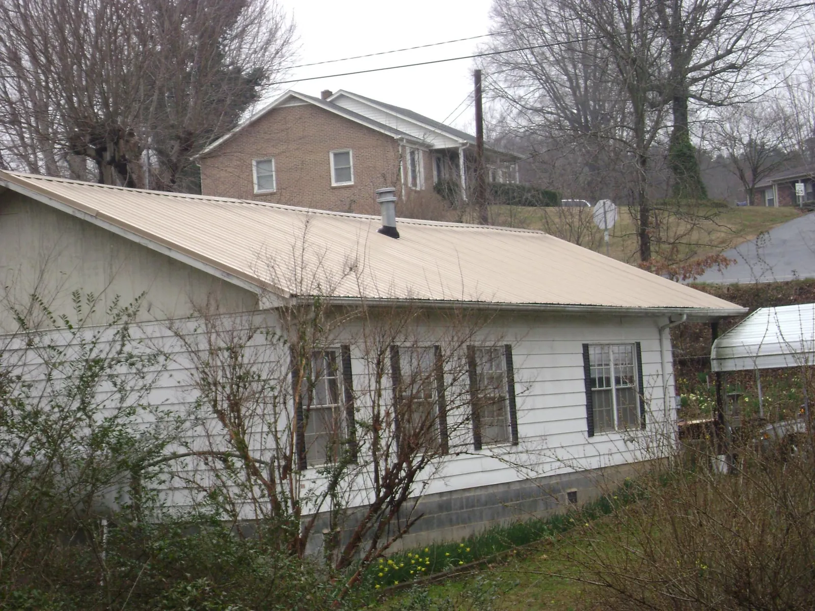 Tan metal roof on a white sided house set into a hillside — Commercial Roofing by Roofing Brothers in Tremont City